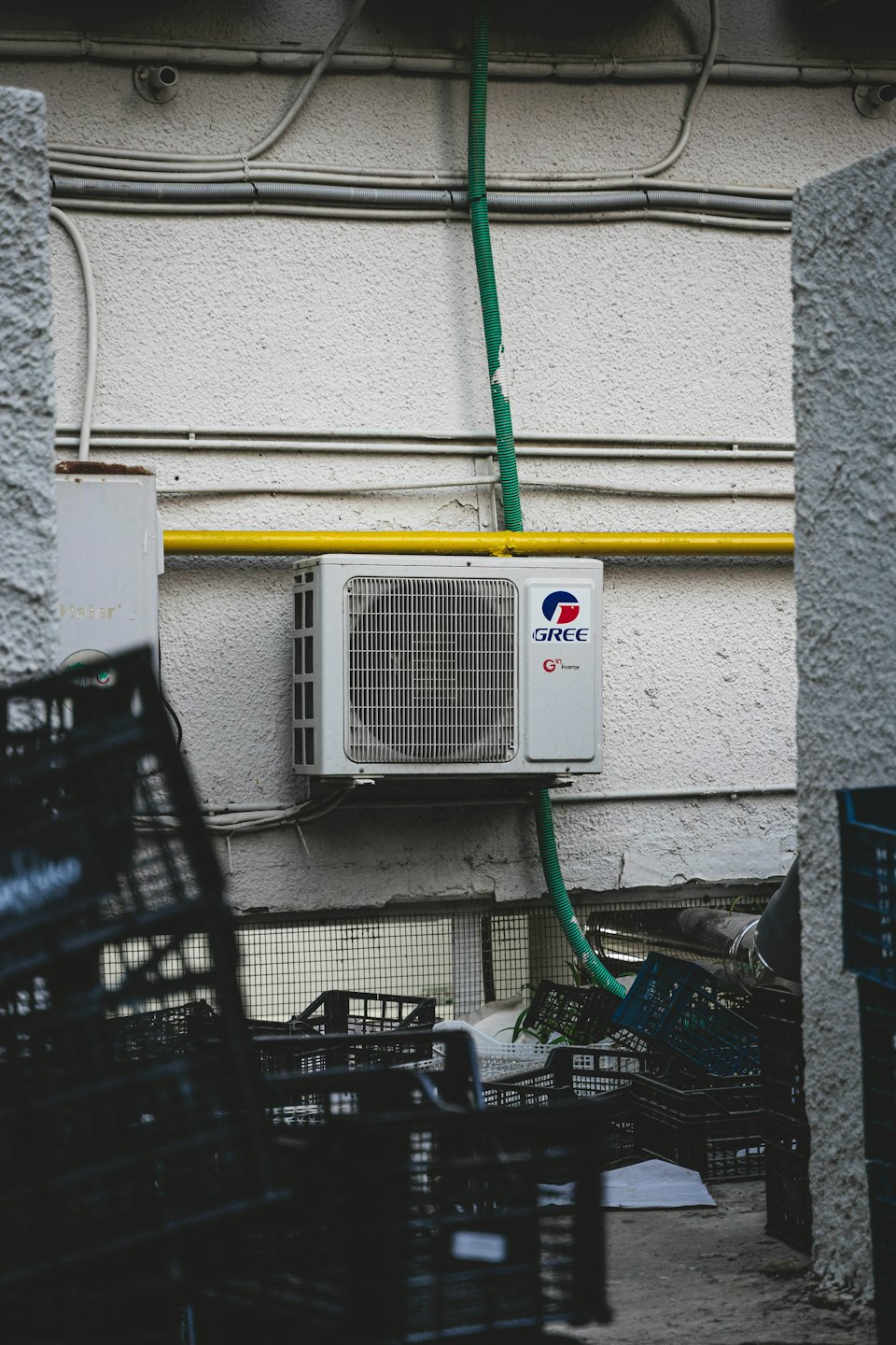 Unità esterna di un condizionatore montata su un muro bianco con tubo giallo.