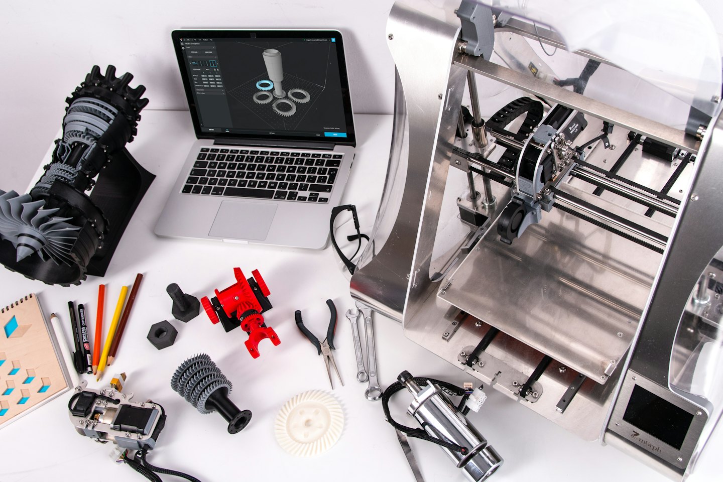 Stampante 3D e laptop su una scrivania bianca con prototipi.